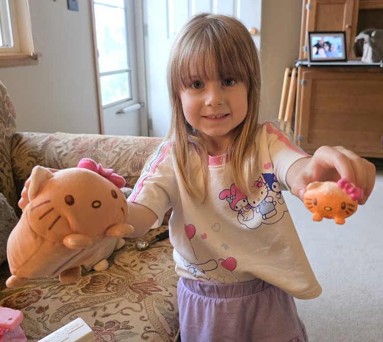 A child holding the original plush cat in one hand and its painted mini twin in the other