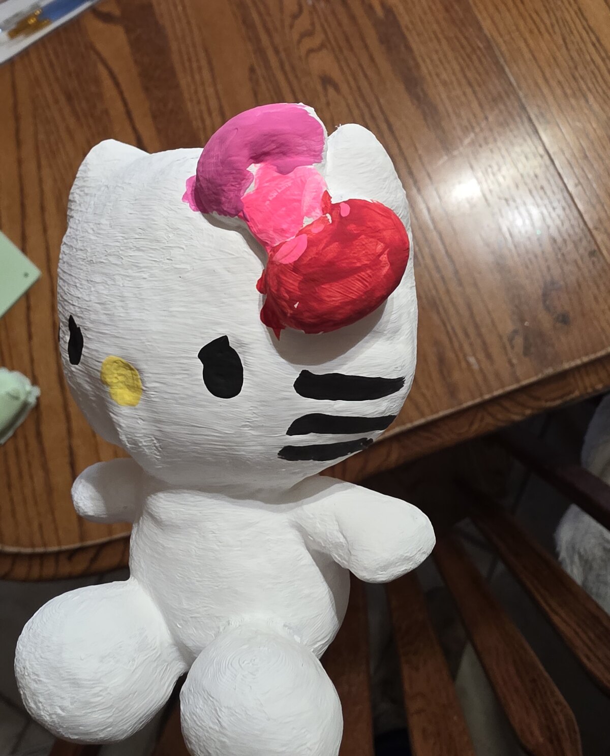 A white 3D-printed cat mini being hand-painted, its bow half pink and red