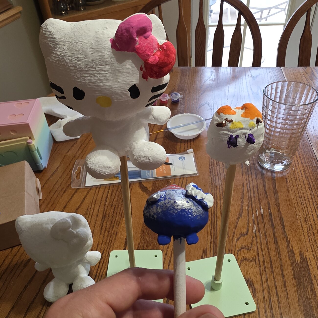 A hand holding a stand of freshly printed minis being hand-painted on craft sticks
