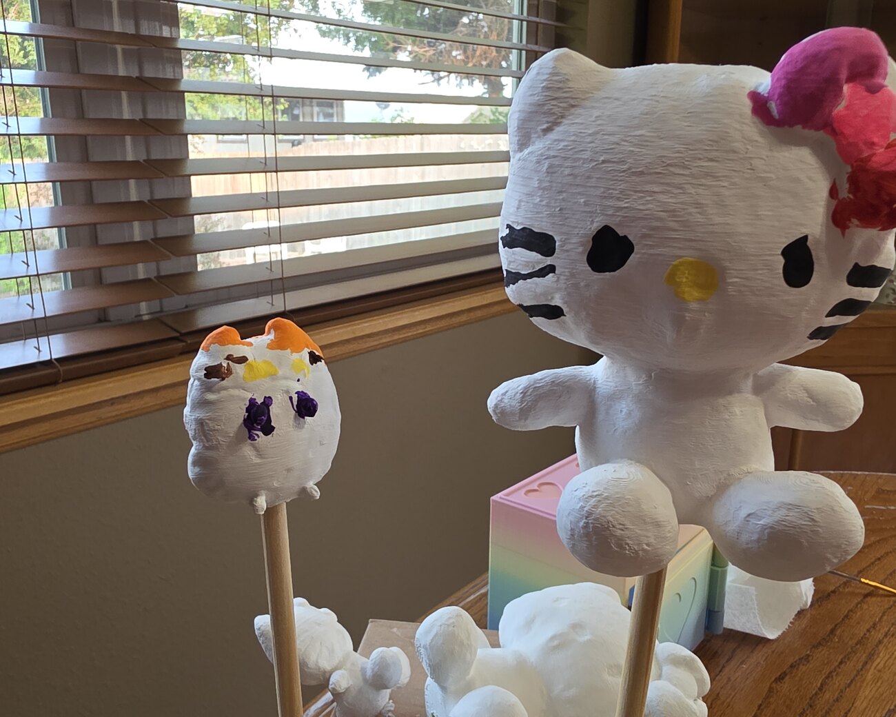 A cat mini and a small painted figurine on a stick, mid-paint by a sunny window