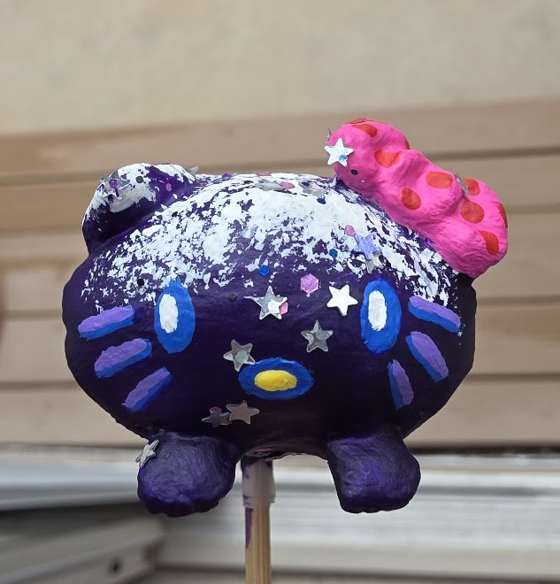 A Loaf Kitty mini painted as a glittery purple galaxy with a pink bow, front view