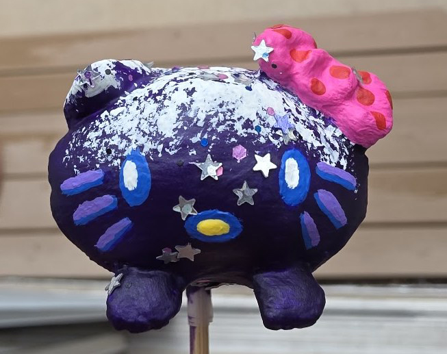 A finished mini painted as a glittery purple galaxy with a pink bow