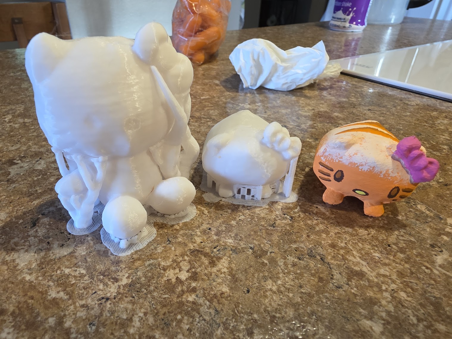 Two raw white 3D prints beside a finished orange-painted mini
